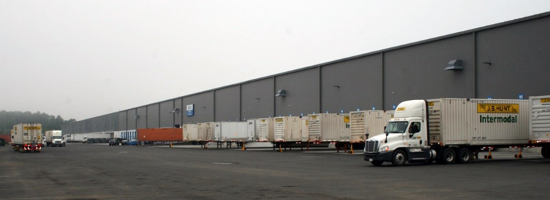 FIGURE 1. Newly Expanded Warehouse with More Than 100 Truck Loading Bays
This image shows truck trailers positioned at loading bays along the side of a modern warehouse. A tractor is attached to one trailer.
FIGURE 1. Newly Expanded Warehouse with More Than 100 Truck Loading Bays
This image shows truck trailers positioned at loading bays along the side of a modern warehouse. A tractor is attached to one trailer.
